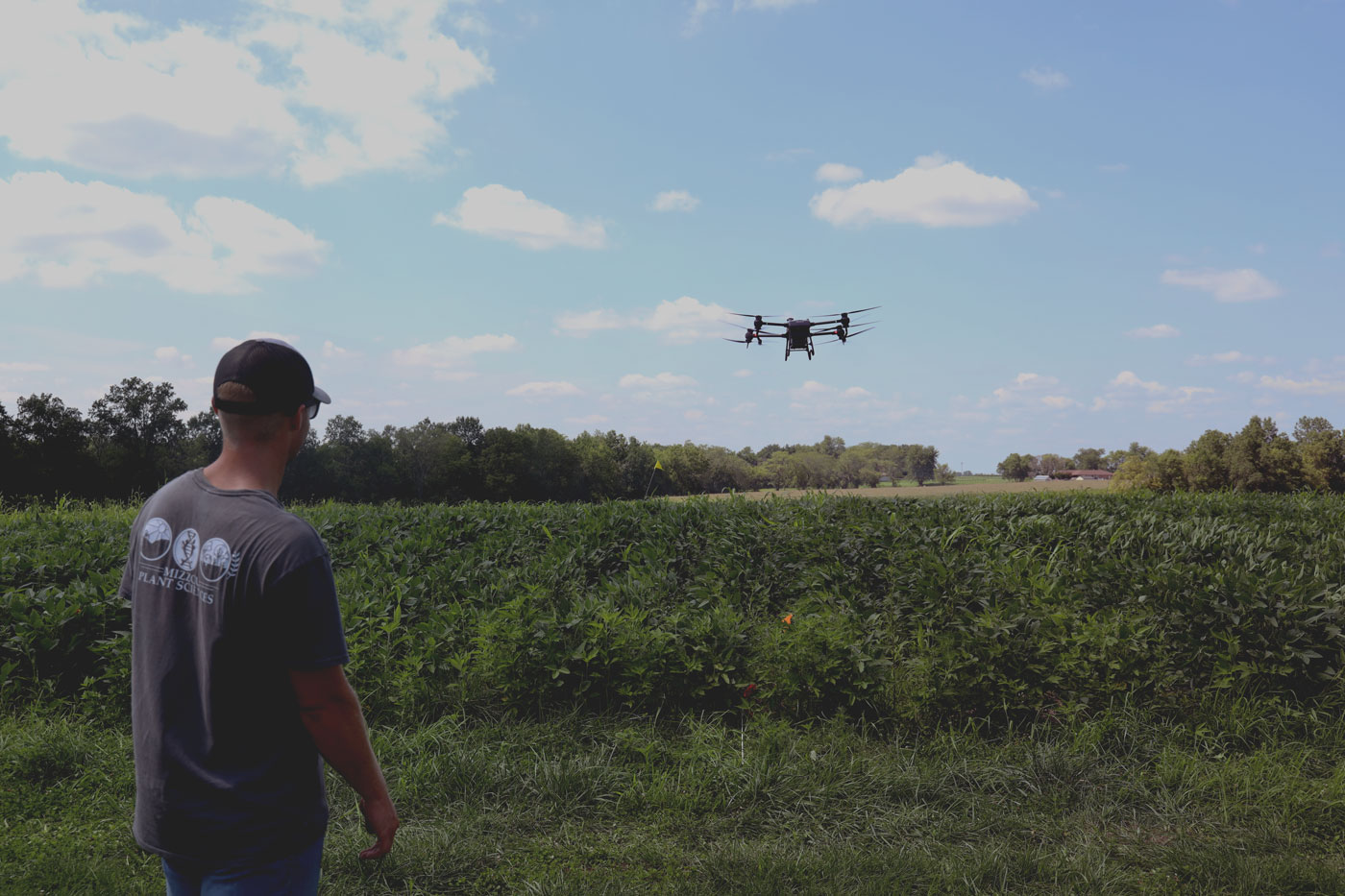 man standing in soybean field with drone hovering above